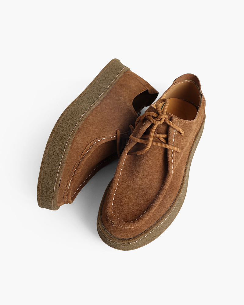 Pair of tan suede moc-toe lace-up shoes with gum crepe soles, one lying on its side, top-down view