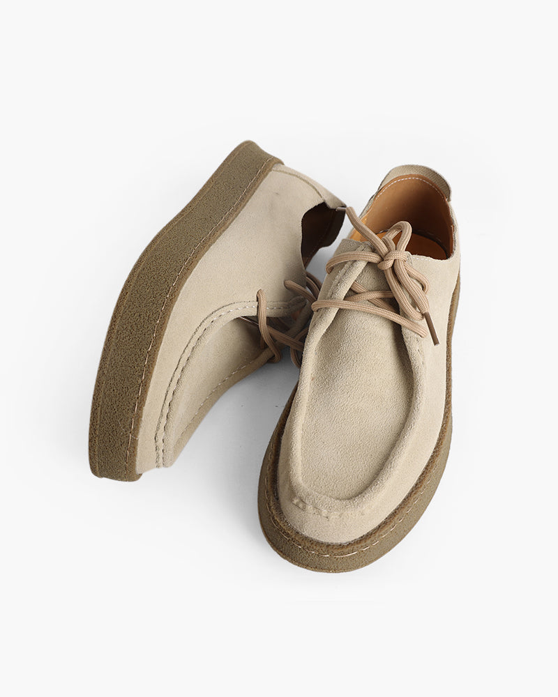 Pair of sand-beige suede moc-toe lace-up shoes with crepe soles, one lying on its side, top-down view