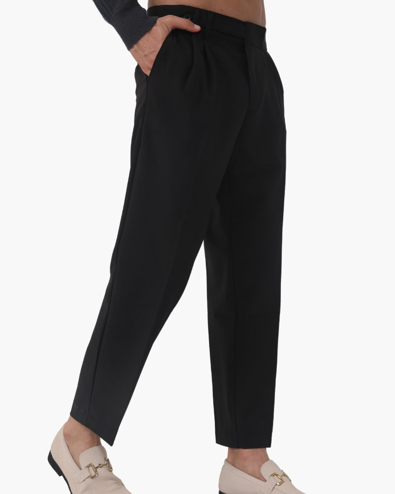 Side view of man in black cropped pleated trousers and cream horsebit loafers, hand in pocket