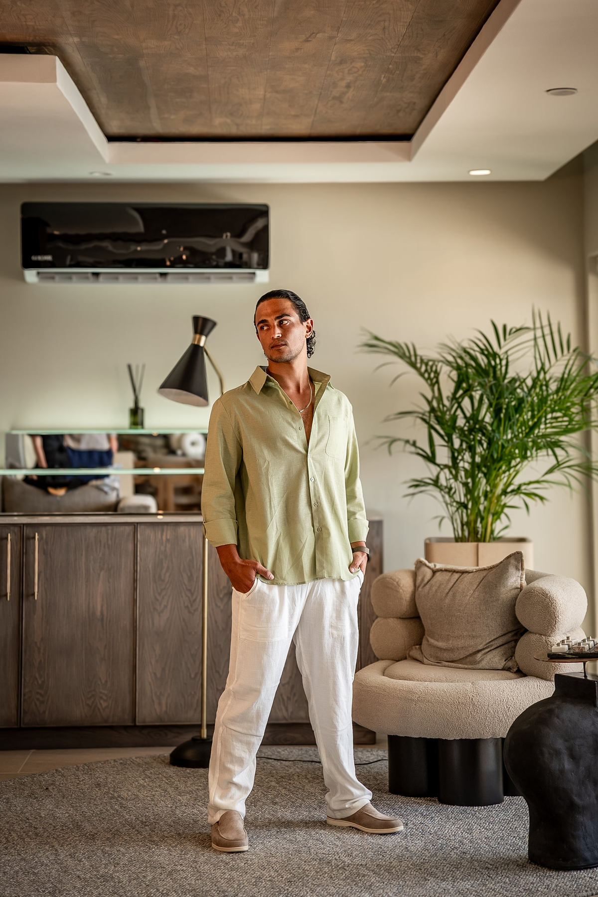 Man in a mint green linen shirt and white trousers standing in a lounge