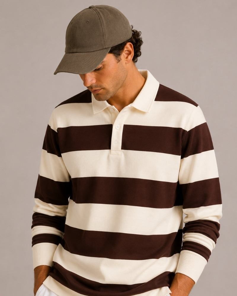 Hombre con polo de rugby a rayas marrón y crudo y gorra verde oliva, mirando hacia abajo, encuadre cerrado