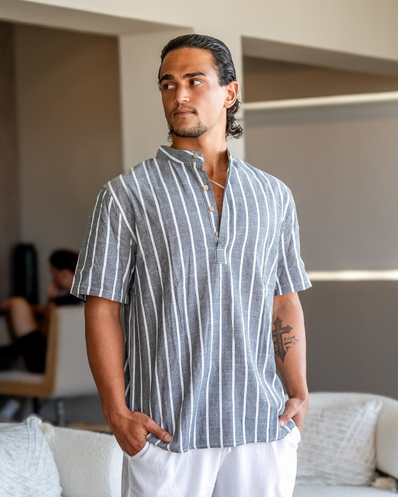 Hombre con camisa de rayas gris de manga corta y cuello mao con pantalón blanco, vista frontal