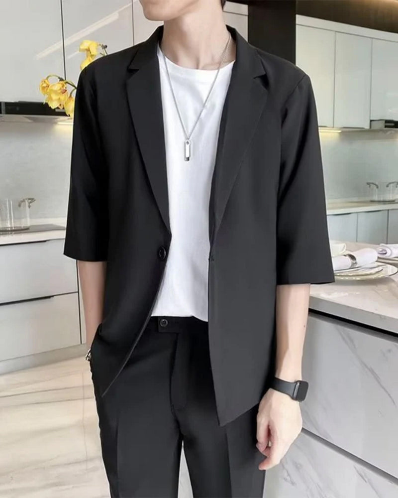Man in black half-sleeve blazer over white tee with pendant necklace, kitchen setting