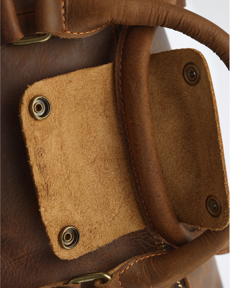 Close-up of leather duffle handle attachment with brass press studs on a suede-lined flap