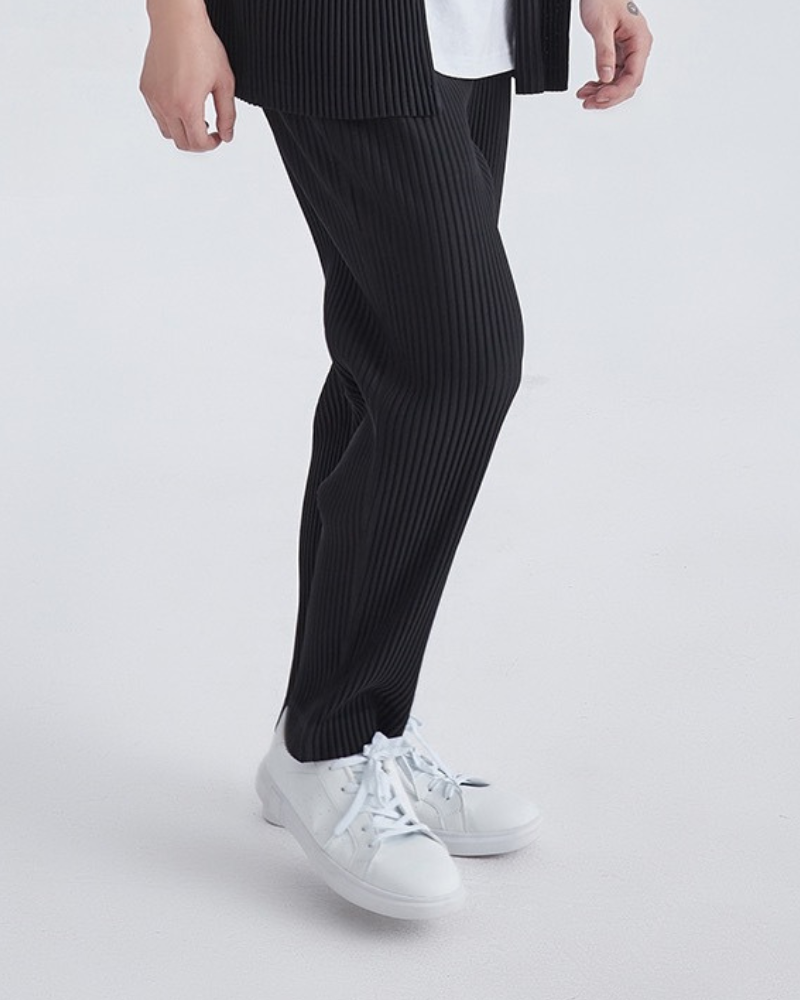 Side view of man in black fine-pleated trousers with white trainers, hand in pocket