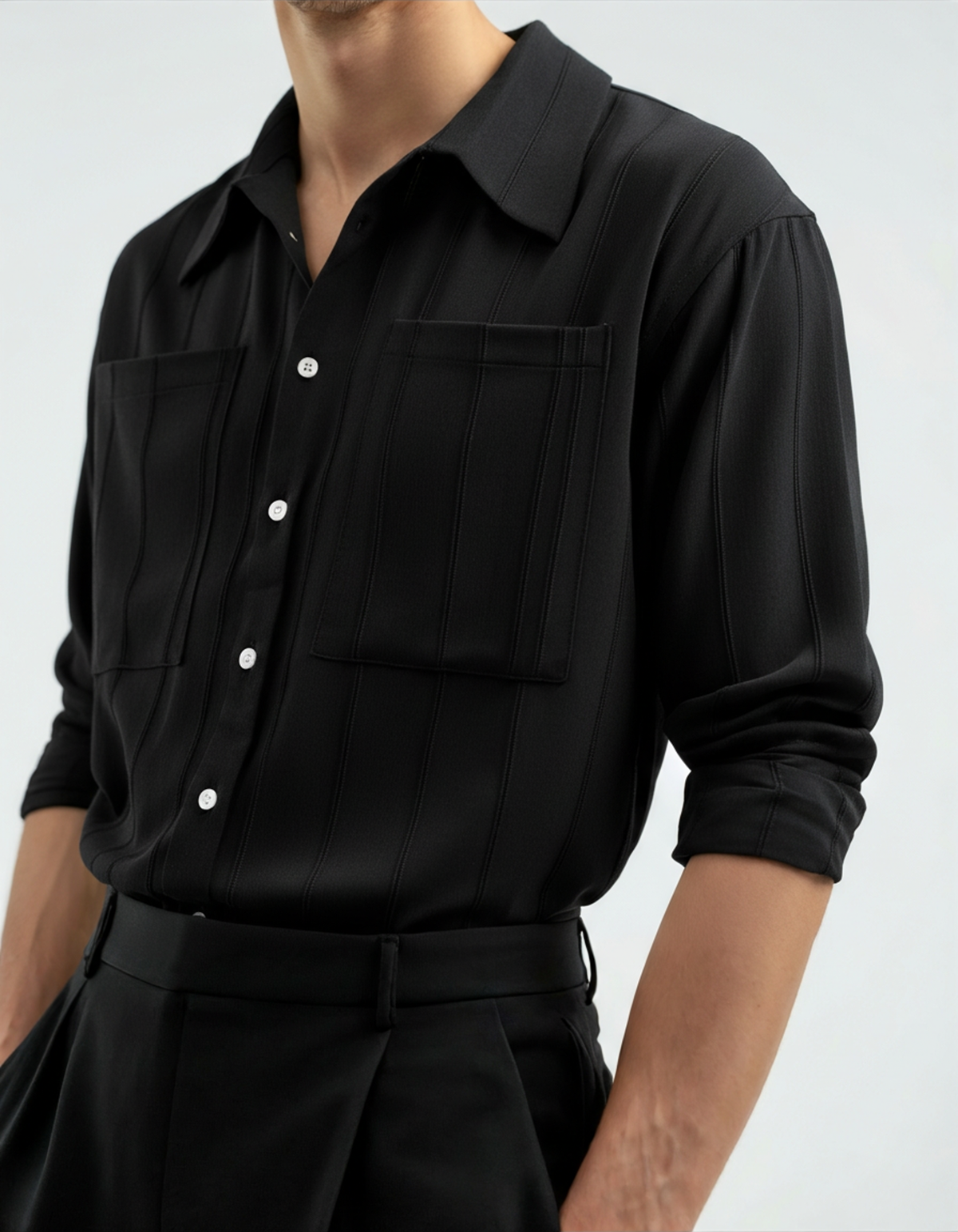 Black vertical-rib shirt with two chest pockets, sleeves rolled, worn with black trousers, front view