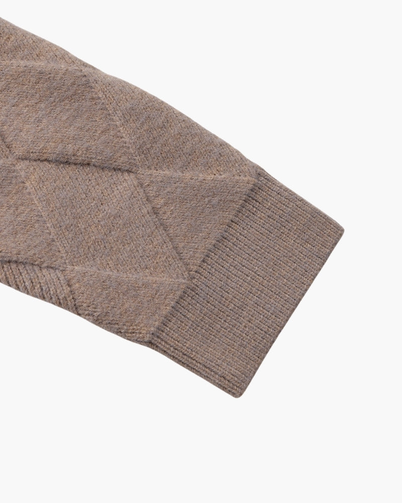 Detalle de la manga de punto de rombos y el puño de canalé de una chaqueta de punto topo