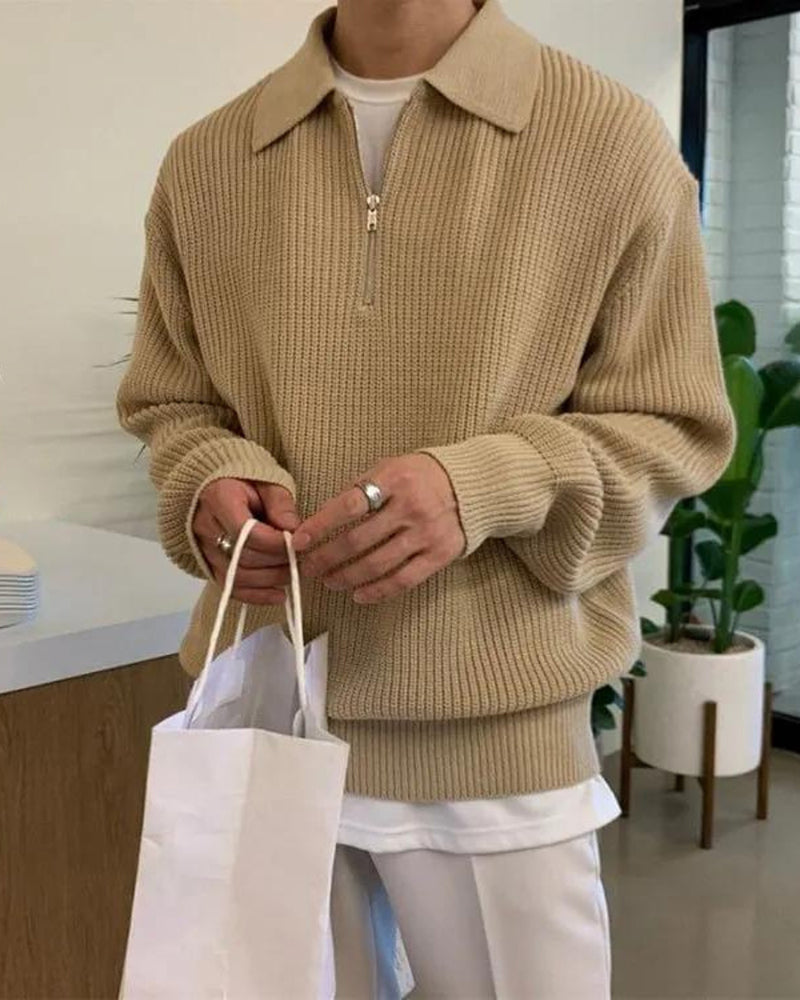 Man wearing beige ribbed half-zip jumper with white trousers, holding a paper bag