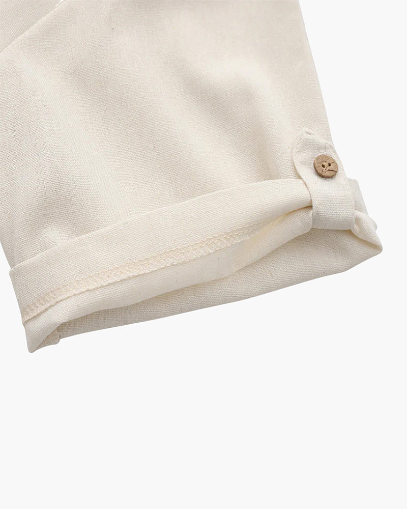 Close-up of a cream linen sleeve rolled up and fastened with a wooden button