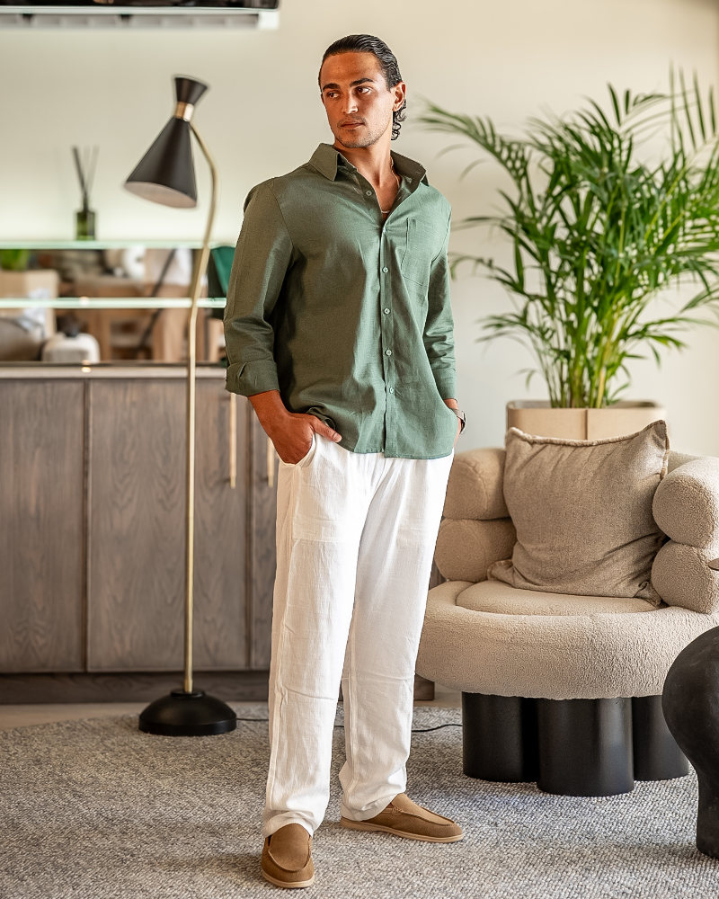 Man in a green long-sleeve linen shirt and white linen trousers standing in a lounge