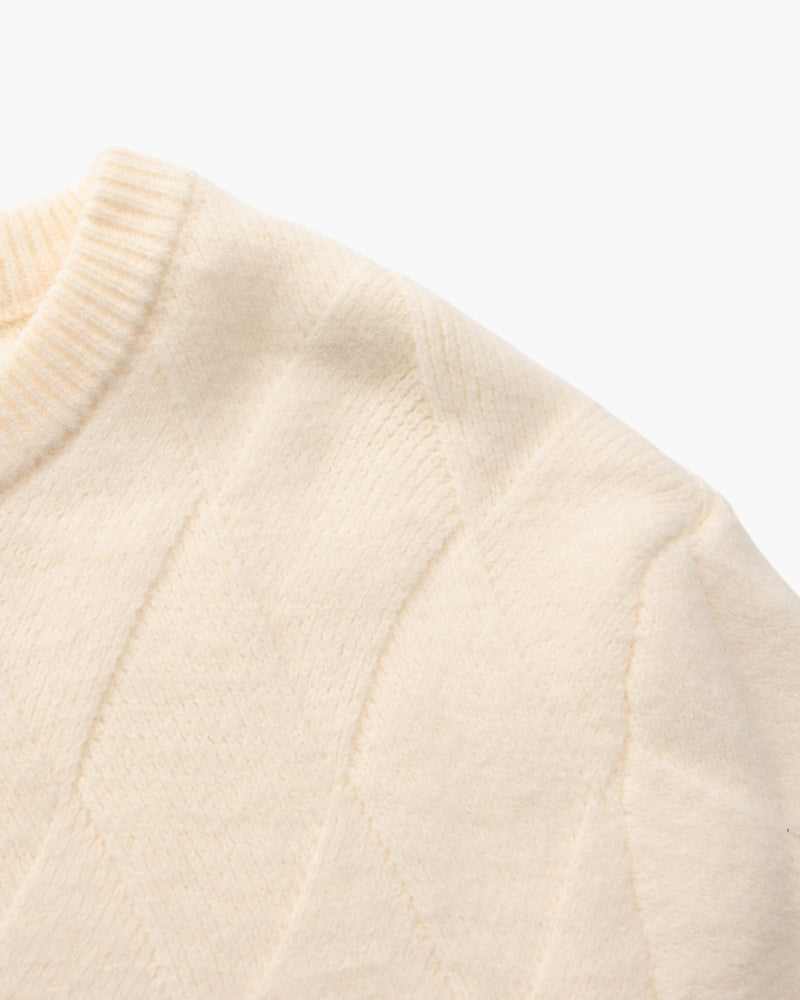 Gros plan sur l'épaule et l'encolure d'un pull crème en maille losange