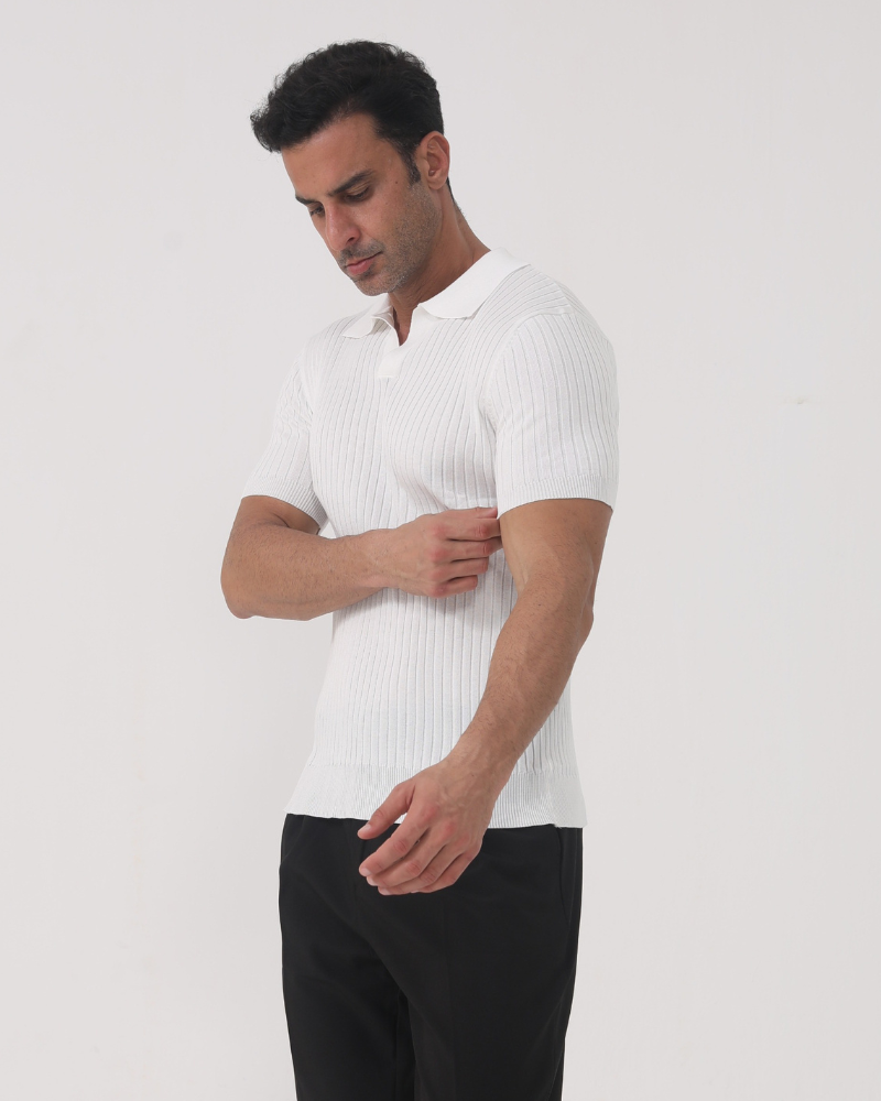 Man in white ribbed knit polo, head turned down, adjusting cuff against grey backdrop