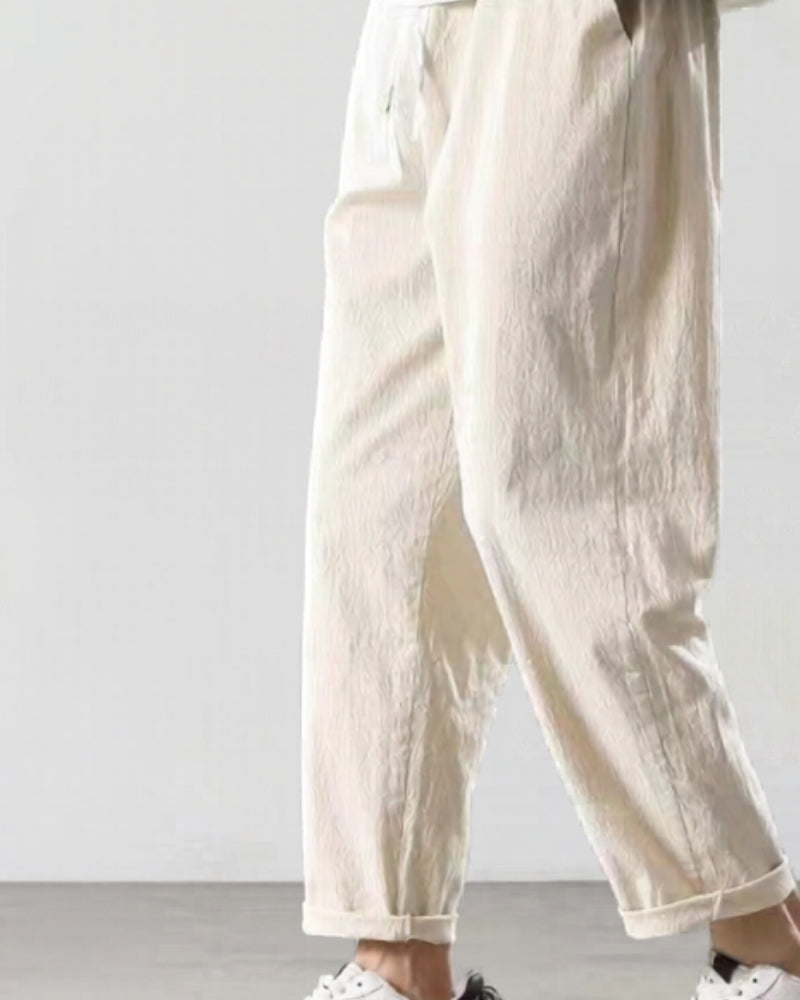 Man in cream linen drawstring trousers with rolled hems and white trainers, side view
