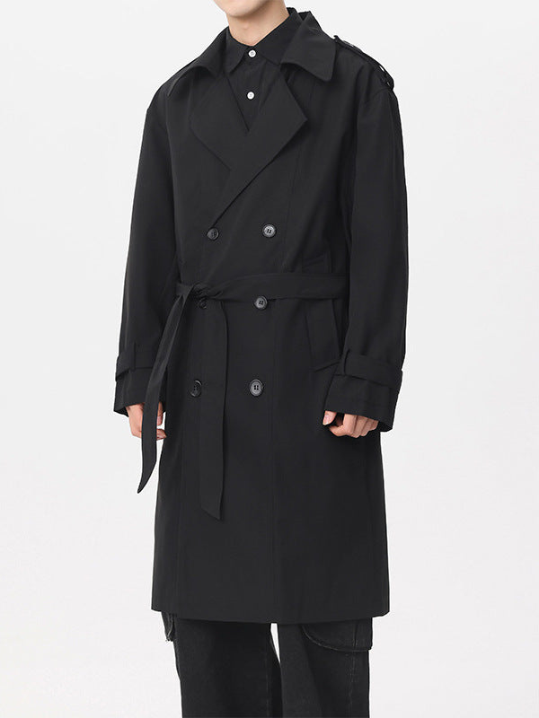 Man in a black double-breasted trench coat with belt and epaulettes, front view with black trousers