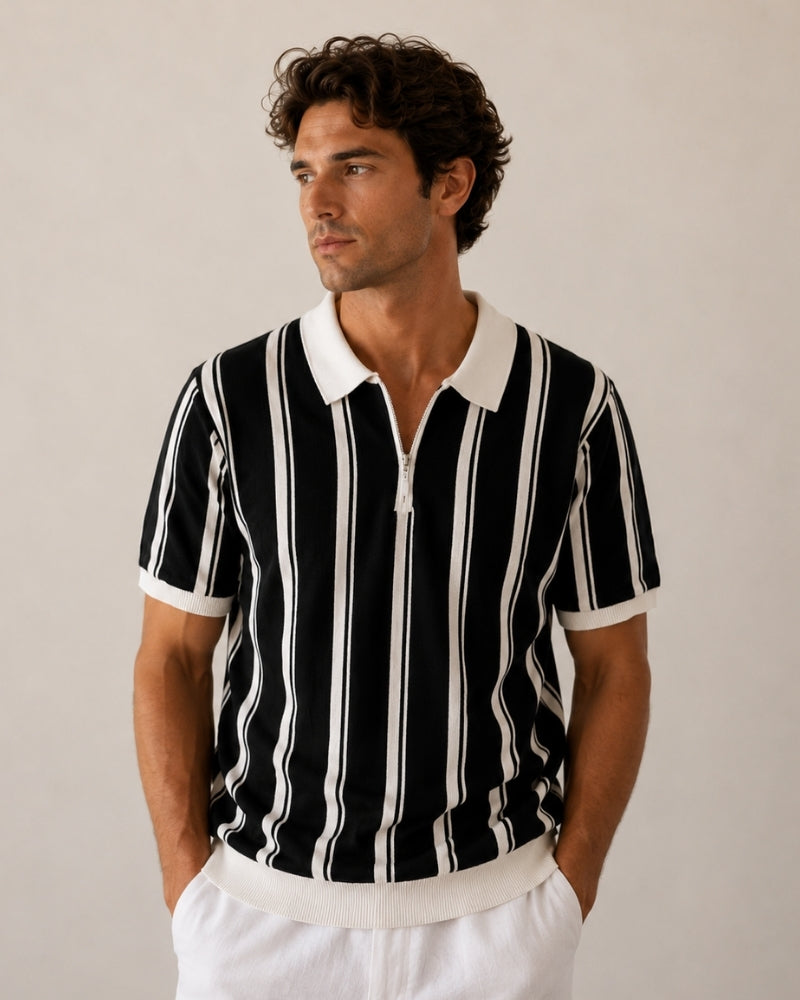 Man in black knit zip polo with white vertical stripes and white collar, hands in white trouser pockets