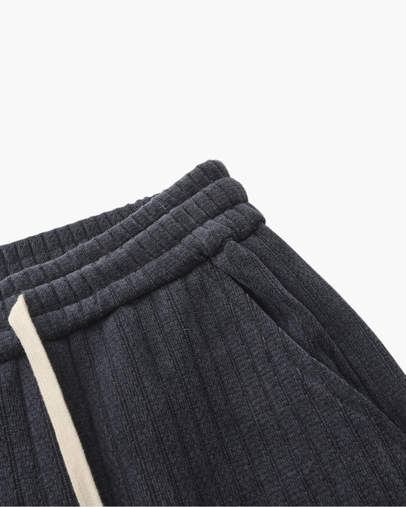 Close-up of charcoal-grey ribbed velvet trousers elastic waistband and side pocket, angled flat-lay