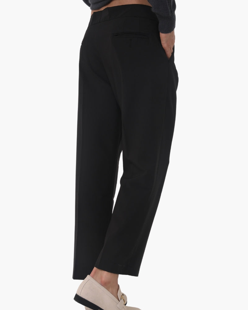 Rear three-quarter view of black pleated trousers with jetted back pocket, cream loafers, white background