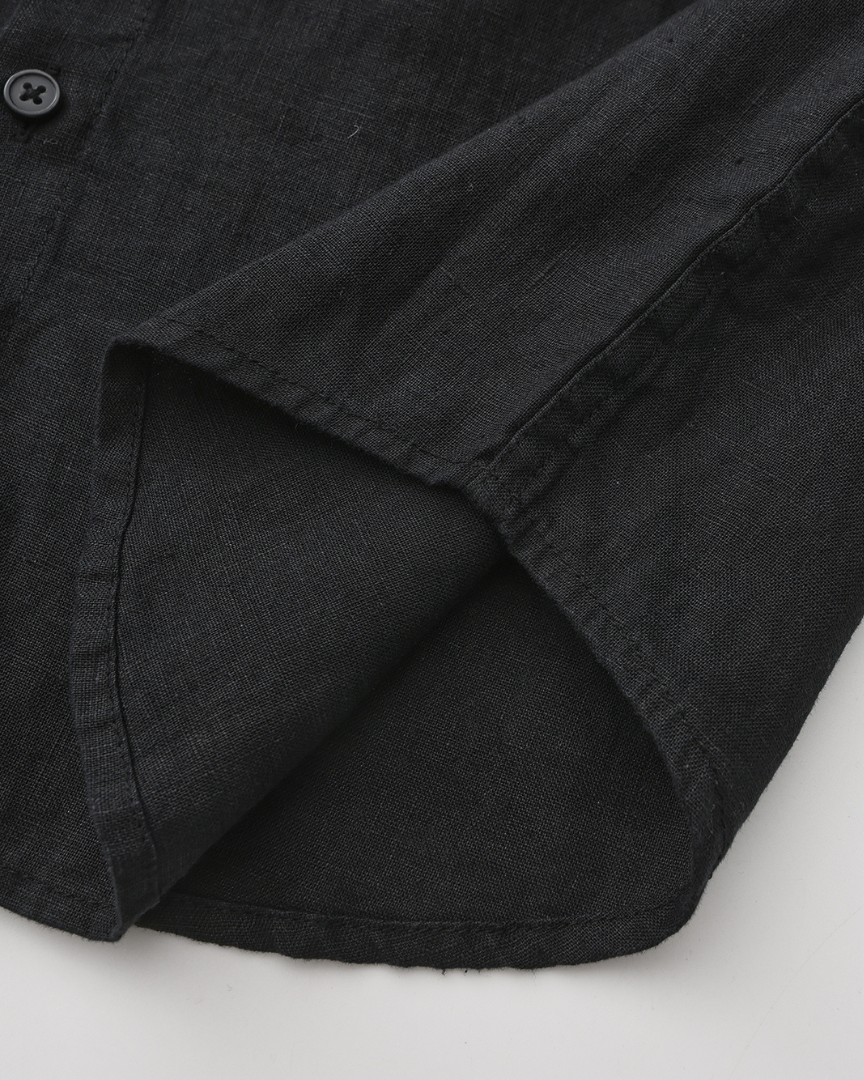 Close-up of black linen shirt curved hem with stitched edge and side seam, one matt button visible