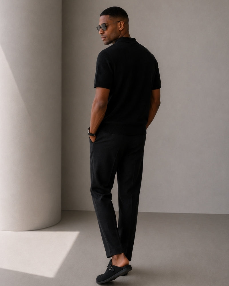 Back view of man in black knit zip polo and black trousers with loafers