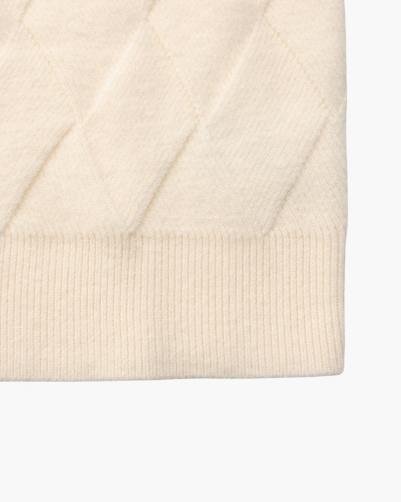 Gros plan sur l'ourlet côtelé d'un pull crème en maille losange