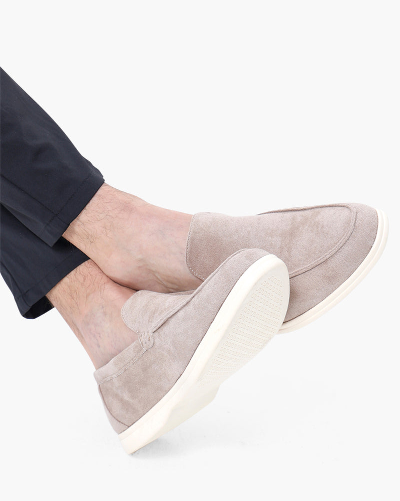 Mocasines de ante topo claro con suela blanca y pantalón azul marino, piernas cruzadas, primer plano