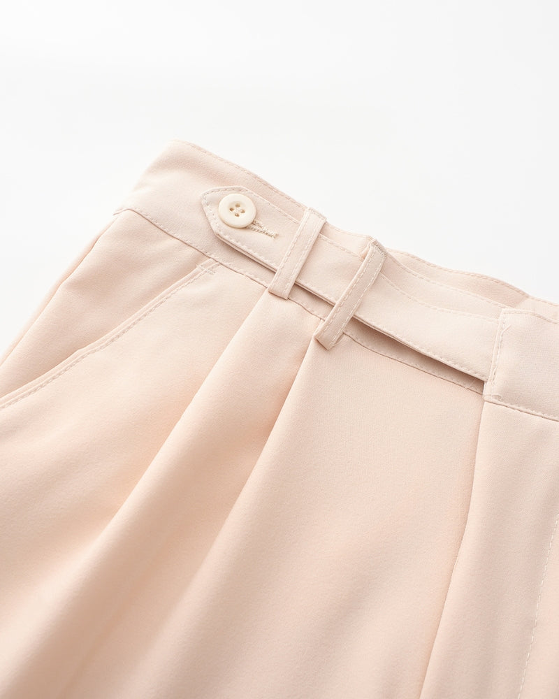 Close-up of beige-pink trousers waist with side-adjuster button tab and double pleats