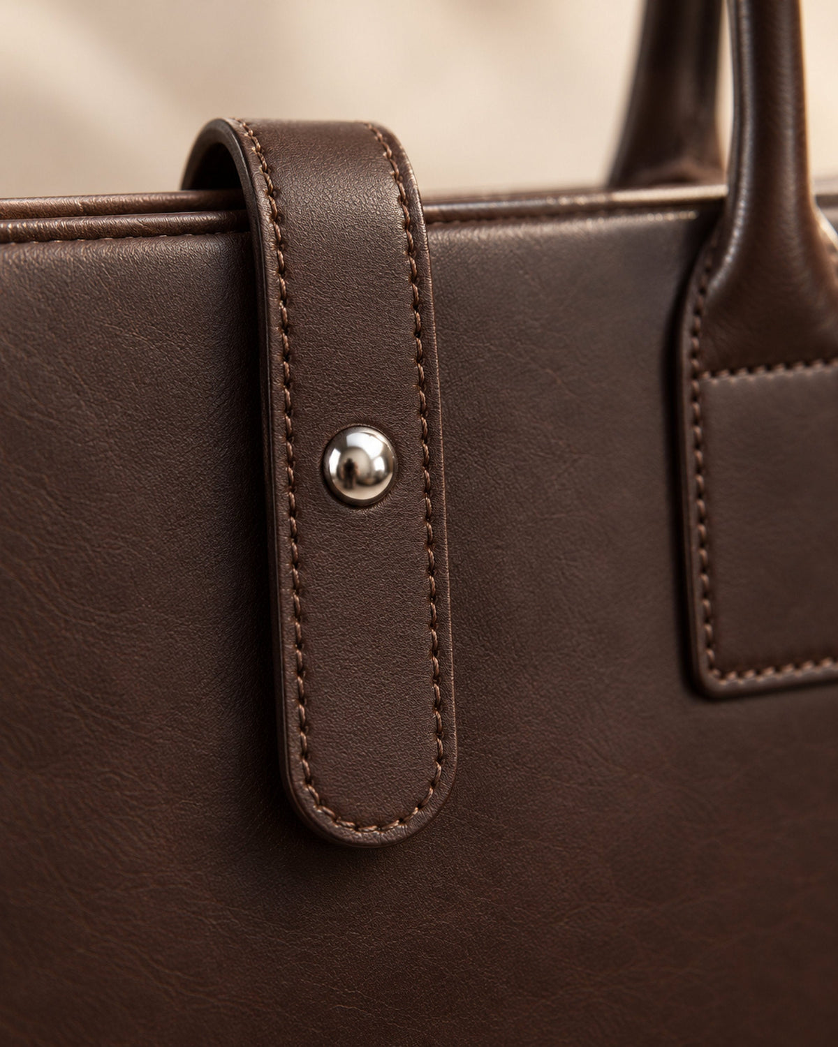 Close-up of a briefcase leather tab with silver stud and stitched top handle