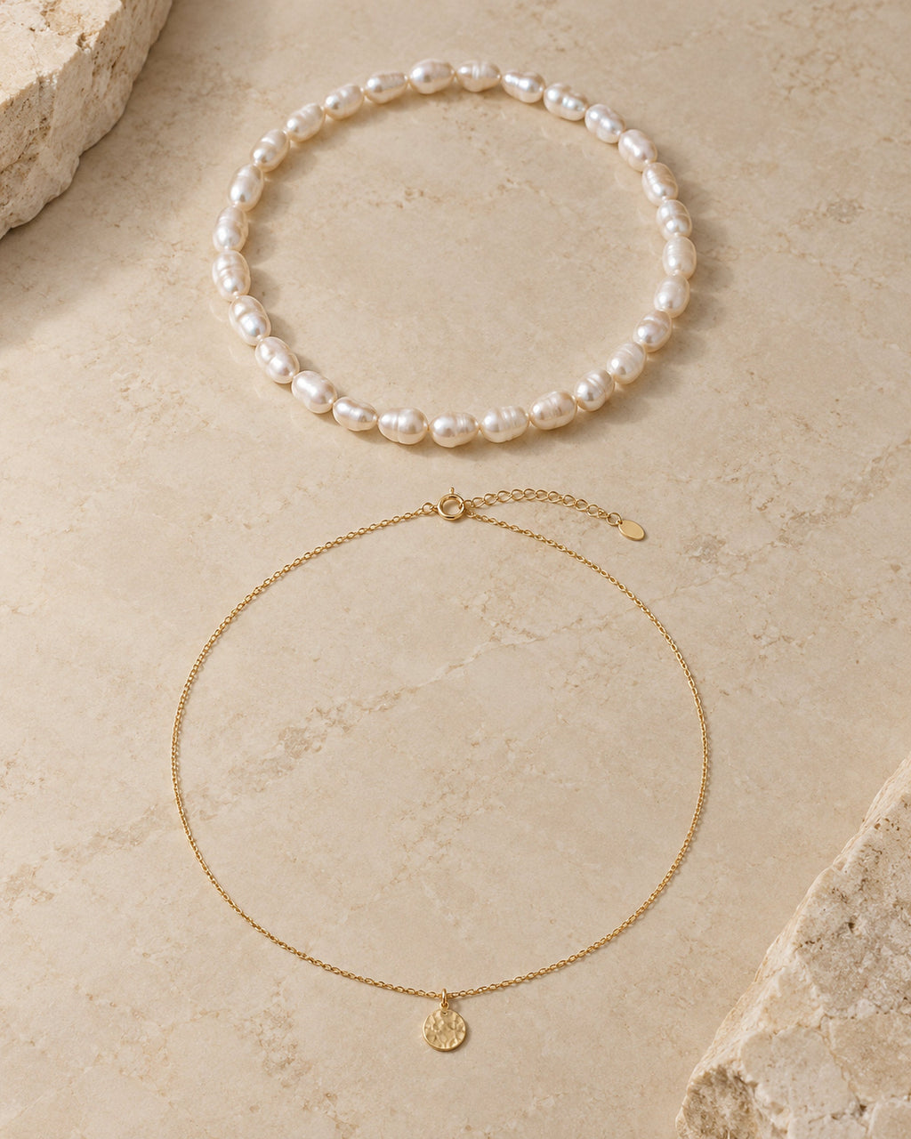 Gargantilla de perlas y collar con colgante de moneda dorado en plano sobre piedra clara