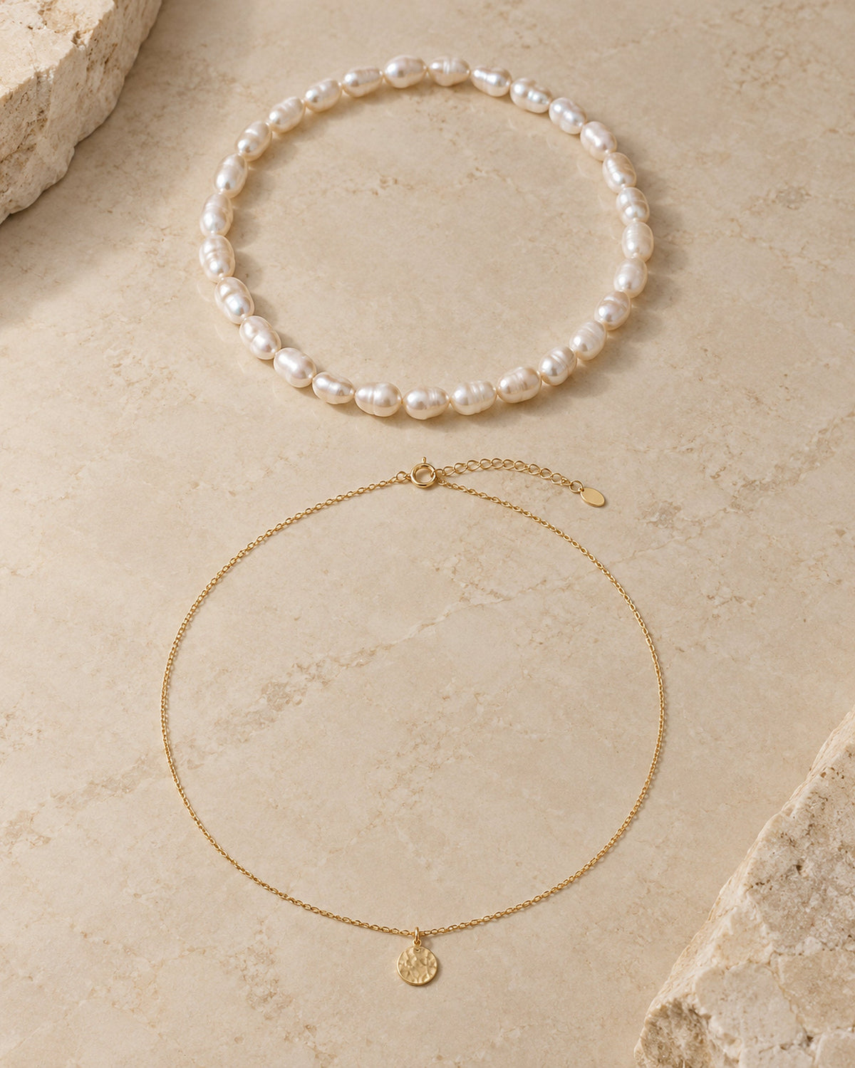 Gargantilla de perlas y collar con colgante de moneda dorado en plano sobre piedra clara