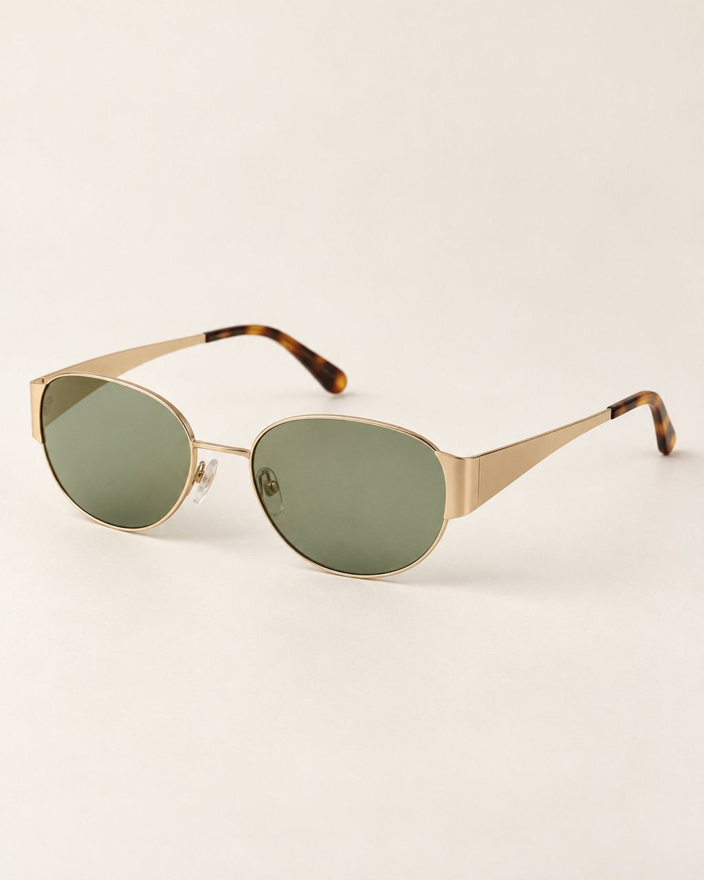 Gold-tone oval sunglasses with green lenses and tortoiseshell tips, angled view on a beige surface