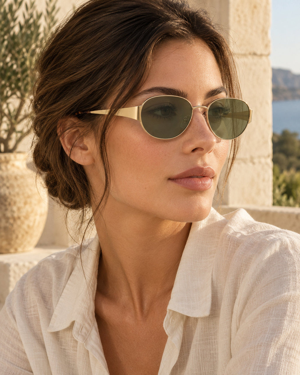 Woman wearing oval gold-frame sunglasses with green lenses, side profile, white linen shirt
