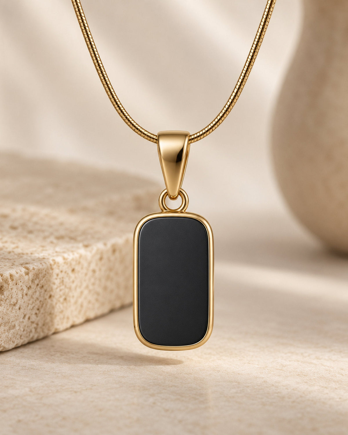 Close-up of black rectangular pendant in a gold frame on a gold-tone snake chain