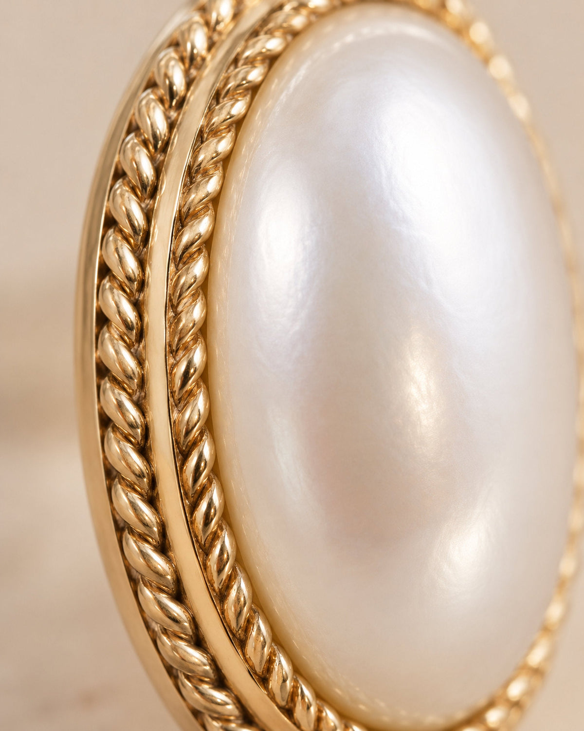 Extreme close-up of an oval pearl stud with gold-tone twisted rope and smooth gold border