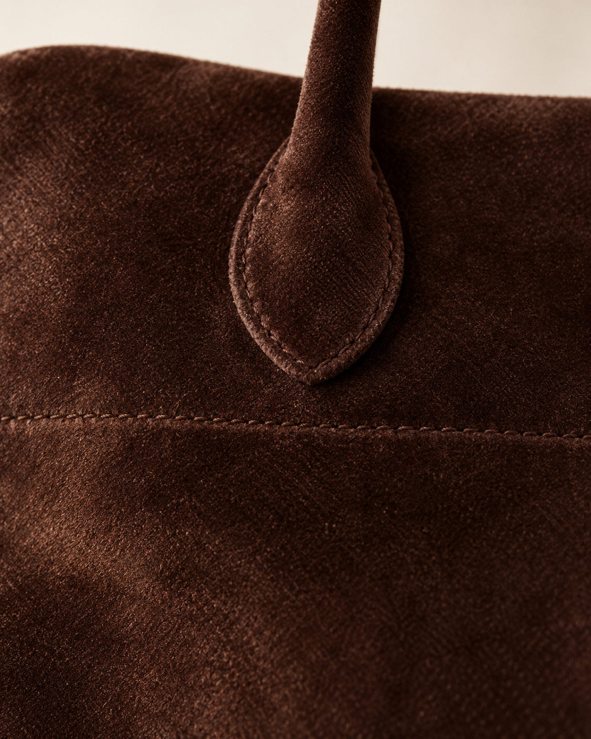 Close-up of dark brown suede-look handbag handle tab and top stitching